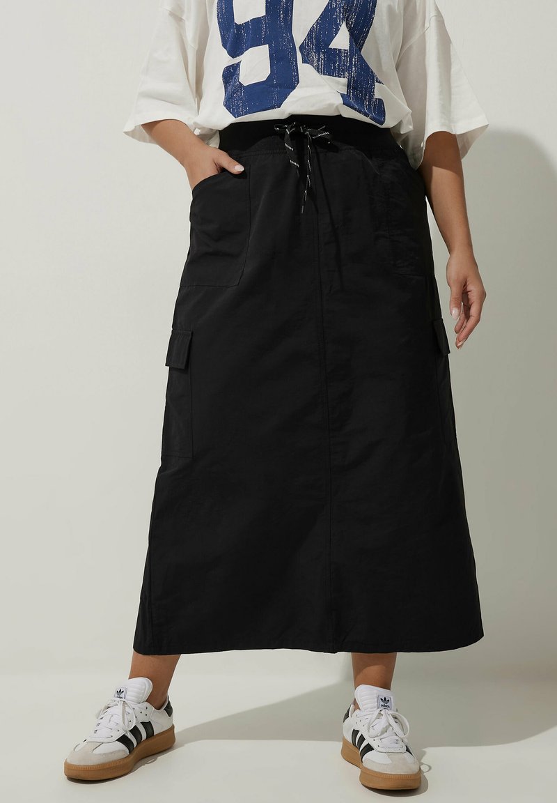 Svart cargokjol med dragsko i midjan, sidofickor och rak silhuett. Kombinerad med vita sneakers med svarta ränder.