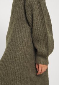 Stickad klänning i olivgrön, med ribbat mönster, långa puffärmar och en avslappnad passform. Mjuk tyg med en mysig känsla.