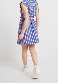 Gestreiftes Kleid mit blauen, roten und weißen vertikalen Streifen, kurzen Ärmeln, tailliertem Gürtel und ausgestelltem Rock.