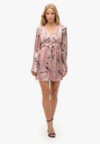 Vestido floral rosa con diseño cruzado, mangas largas y cintura elástica. Presenta patrones florales negros sobre una textura similar a la seda.