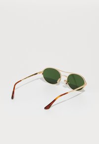 Gafas de sol con marco de metal dorado y lentes verdes, de forma ovalada alargada, y brazos con patrón de carey. Incluyen almohadillas nasales ajustables.