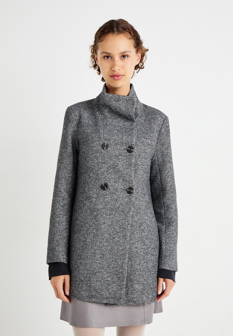 Manteau double boutonnage gris texturé avec col haut, boutons noirs et poignets noirs contrastants. Le tissu semble chaud et robuste.