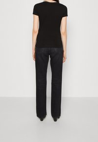 Sort, tætsiddende T-shirt med korte ærmer parret med mørk vaskede lige ben jeans. Stoffet ser glat ud med minimal synlig syning.