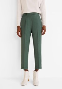 Groene geplooide broeken van een zachte stof, met een hoge taille en cropped lengte, gecombineerd met witte hoge enkelschoenen.