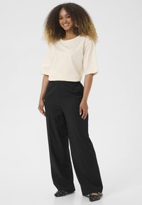Crème blouse met korte mouwen, versierd met kleine embellissementen; gecombineerd met zwarte high-waisted wijde broek en instap schoenen.