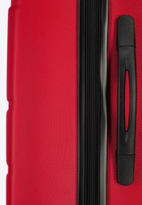 Maleta roja con una superficie texturizada, cierre negro con cremallera y un asa negra en el lateral para llevarla.