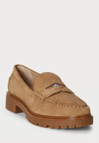 Tan suede loafer with a round toe, featured stitching, and a branded accent. Thick brown rubber sole adds durability and traction.