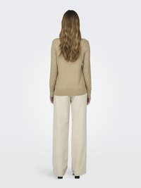 Pull beige à manches longues avec un ourlet arrondi, associé à un pantalon large taille haute en crème clair. Texture douce, manches ajustées.
