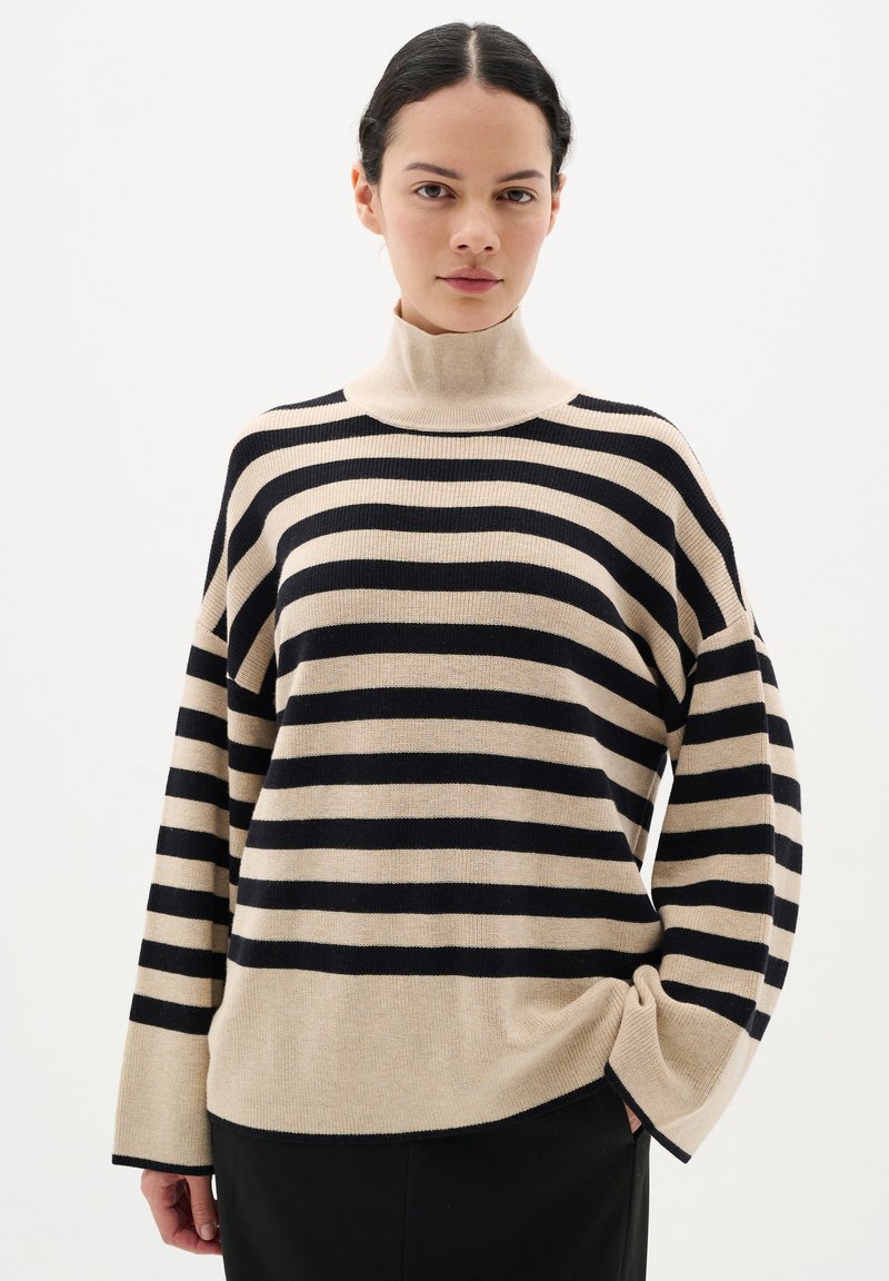 Maglione beige con ampie strisce blu navy, colletto alto, vestibilità ampia e maniche lunghe. Morbida texture e polsini a costine.