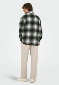 Camisa de cuadros en verde, negro y blanco con mangas largas y puños abotonados. Llevada con pantalones beige y zapatillas blancas.