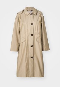 Μπεζ παλτό τύπου trench με δομημένο σώμα, μεγάλους μπροστινούς κουμπιά, δύο πλαϊνές τσέπες και κουκούλα με κορδόνι. Λεπτό ύφασμα με ελαφριά γυαλάδα.