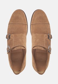 Suede braune Schuhe mit zwei silbernen Schnallen, abgerundetem Zehenbereich, flacher Sohle und genähten Details auf dem Obermaterial, im Design für einfaches Hineinschlüpfen.
