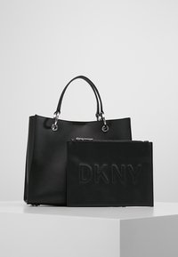Czarna skórzana torba typu tote z dwoma uchwytami i zapinanym na zamek saszetką z wytłoczonym logo "DKNY", gładką fakturą i błyszczącymi elementami ozdobnymi.