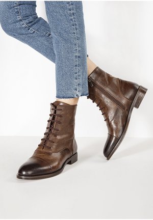 Bottes basses en cuir marron avec une surface texturée, des lacets à l'avant et une fermeture éclair latérale, posées sur un fond clair.