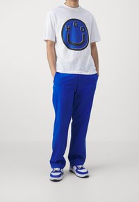 Camiseta de algodón blanca con logotipo gráfico azul, combinada con pantalones de algodón azules y zapatillas azul y blancas. Ajuste simple y relajado.