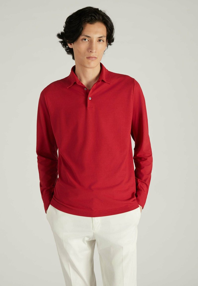 Rode lange mouwen polo met een kraag en een drieknopen sluiting, gecombineerd met lichte broek; gladde textuur.