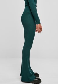 Teal ribbelgebreide jumpsuit met uitlopende benen, strakke pasvorm en lange mouwen. Verstelbare halslijn en zwarte plateau schoenen.