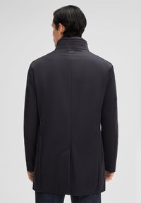 Donker marineblauwe jas met een hoge kraag, een gladde textuur en minimale naden. Heeft een enkele vent aan de achterkant en geen zichtbare hardware.