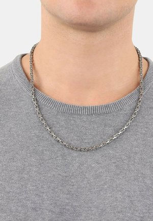 Collana in argento con maglie rettangolari, posizionata su un maglione di lana grigio. Il materiale appare lucidato con una superficie liscia.