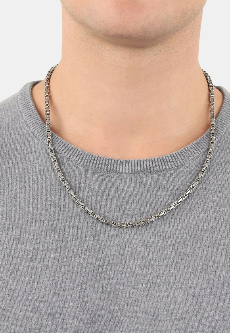 Collana in argento con maglie rettangolari, posizionata su un maglione di lana grigio. Il materiale appare lucidato con una superficie liscia.