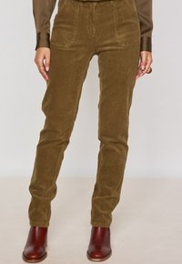 Pantaloni in velluto a coste marroni con righe verticali, tasche frontali e vestibilità slim, abbinati a stivaletti con tacco marroni.