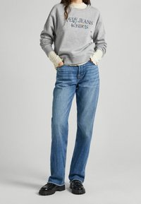 Šedá mikina s výšivkou "Pepe Jeans London", spárovaná s světle modrými rovnými džíny a černými platformovými botami. Krémová košile pod ní.