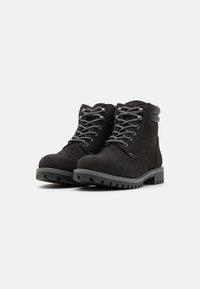 Botas de tobillo de ante negro con cordones grises, punta redonda, suela de goma gruesa y cuello acolchado que presenta una textura suave y un diseño robusto.
