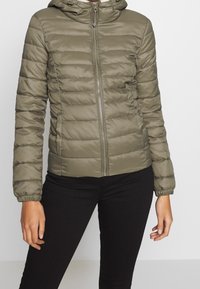 Oliwkowa puchowa kurtka z zamkiem z przodu, kapturem i elastycznymi mankietami. Charakteryzuje się poziomym pikowaniem i gładką teksturą nylonu.