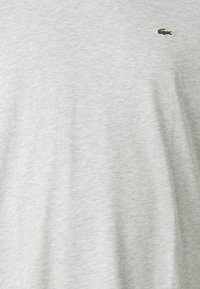 Tricou din bumbac gri cu mâneci scurte și un finisaj texturat subtil. Prezintă un mic logo brodat verde pe partea stângă.