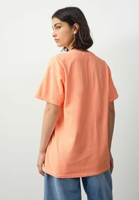 Løst siddende kortærmet t-shirt i blød koralfarvet bomuld, med rund halsudskæring og simpel kant, parret med lyseblå denimjeans.