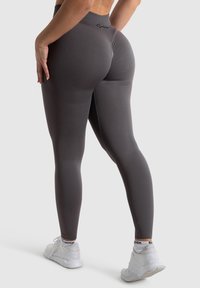 Hochtaillierte graue Leggings mit glattem, dehnbarem Material; Logo am Bund; kombiniert mit weißen Sportschuhen.