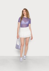 Top roxo transparente com padrões ondulados, saia mini branca em camadas, mala lilás e ténis claros. Texturas suaves em toda a parte.