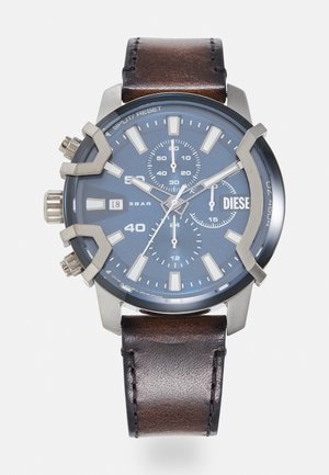 Chronograph-Uhr mit Zifferblatt in Dunkelblau, Gehäuse aus silberfarbigem Edelstahl und braunem Lederarmband mit strukturierten Oberflächen und Metallakzenten.