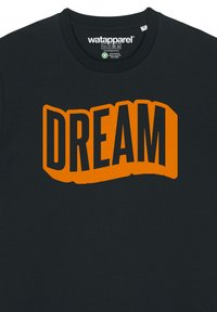 Zwarte katoenen T-shirt met gedurfde oranje "DREAM" tekst, met een golvend ontwerp en dikke letters, die een soepele textuur toont.