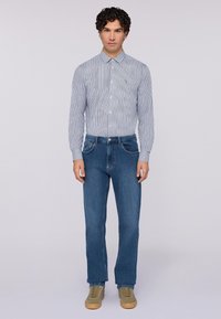 Camicia a maniche lunghe blu e bianca a righe, abbinata a jeans blu in denim e sneakers beige. L'outfit presenta una vestibilità classica e un design semplice.