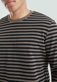 Gestreepte langslijfshirt in zwart en taupe, met een ronde halslijn en ribbelstructuur. De strepen zijn gelijkmatig verdeeld en consistent.