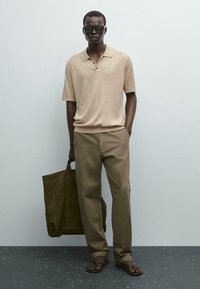 Tan strik polo med ribbet tekstur, beige bukser, brune flip-flops og en mørkebrun tote taske, mod en neutral baggrund.