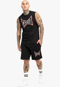 Juodas nesijungiantis marškinėlis ir juodi šortai su raudonu TAPOUT logotipu. Yra sportiško dizaino, pagaminti iš medvilnės, ir kontrastingos baltos kojinės su juostelėmis.