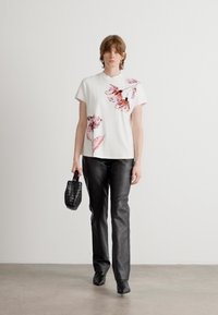 Witte kortslurfshirt met roze bloemenpatroon, zwarte leren broek en een gestructureerde zwarte handtas. Eenvoudige lijnen en moderne silhoutten.