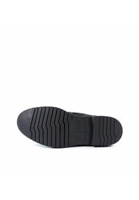 Schwarze Gummisohle mit strukturiertem Profil, das parallele und Zickzack-Rillen aufweist. Gestempeltes Logo und Details in der Nähe der Ferse sichtbar.