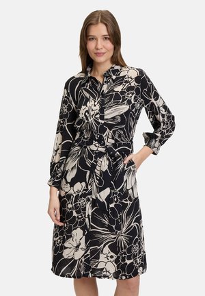 Blumengemustertes Kleid in Schwarz und Beige, mit Kragen, langen Ärmeln, Taillengürtel und Taschen. Glattes Material, knielanges Design.