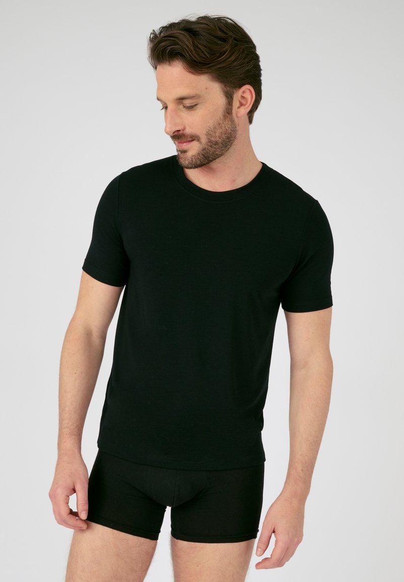 Camiseta negra de manga corta hecha de tejido suave, con cuello redondo y silueta ajustada. Se lleva con calzoncillos boxer negros a juego.
