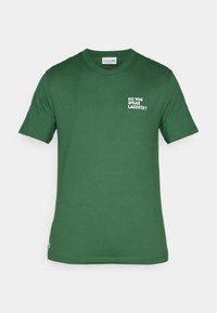 Zelené bavlněné tričko s krátkými rukávy, na kterém se na levé části hrudi nachází bílý potisk s textem "UMÍŠ MLUVIT LACOSTE?" a malé logo poblíž spodního lemu.
