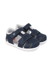 Sandalias de cuero azul marino con acentos blancos, que cuentan con dos correas ajustables de Velcro y diseños troquelados para mayor transpirabilidad. Suela texturizada.