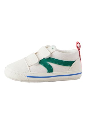 Zapatilla blanca para niño pequeño con franja lateral verde, línea azul en la suela, dos tiras de velcro y lengüeta roja en el talón sobre fondo blanco.