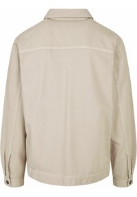 Beżowa kurtka z kołnierzykiem, długimi rękawami, mankietami zapinanymi na guziki i poziomą szwem na górnej części pleców.