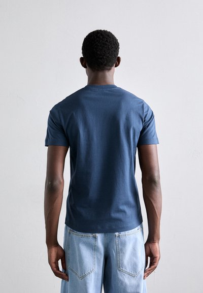 T-shirt en coton bleu marine à manches courtes et col rond. La vue arrière montre une texture lisse et une coupe ajustée associée à un jean bleu clair.
