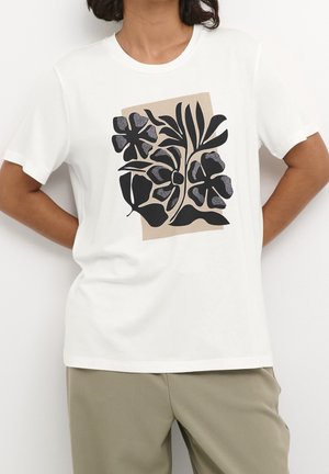Camiseta blanca con un gran estampado floral negro sobre un fondo beige. Mangas cortas, cuello redondo y textura de tela suave.