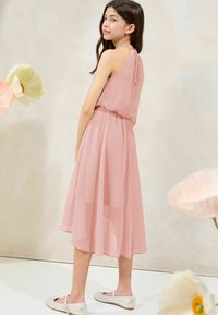 Abito rosa pallido con un design fluido, vita elastica e schiena scoperta. Presenta un tessuto morbido e trasparente e una lunghezza al ginocchio; abbinato a ballerine scintillanti.
