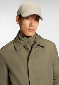 Olivgrüne, leichte Jacke mit hohem Kragen und Reißverschluss, kombiniert mit einer hellgrauen, strukturierten Mütze mit einem gebogenen Schirm.